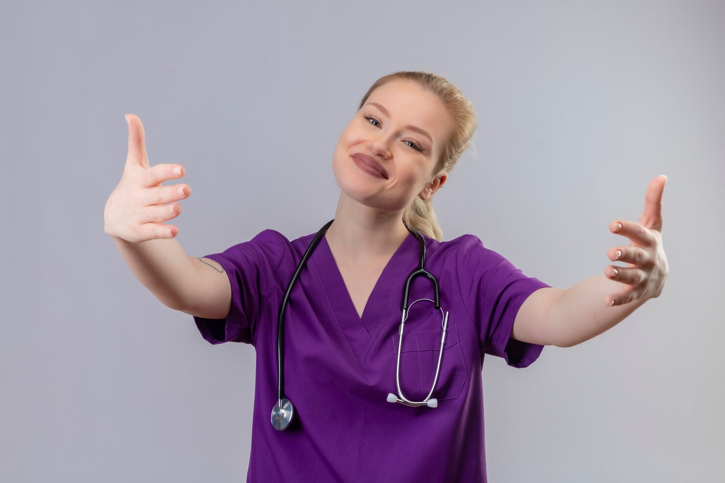 A smiling nurse in blue scrubs checking a woman's blood pressure