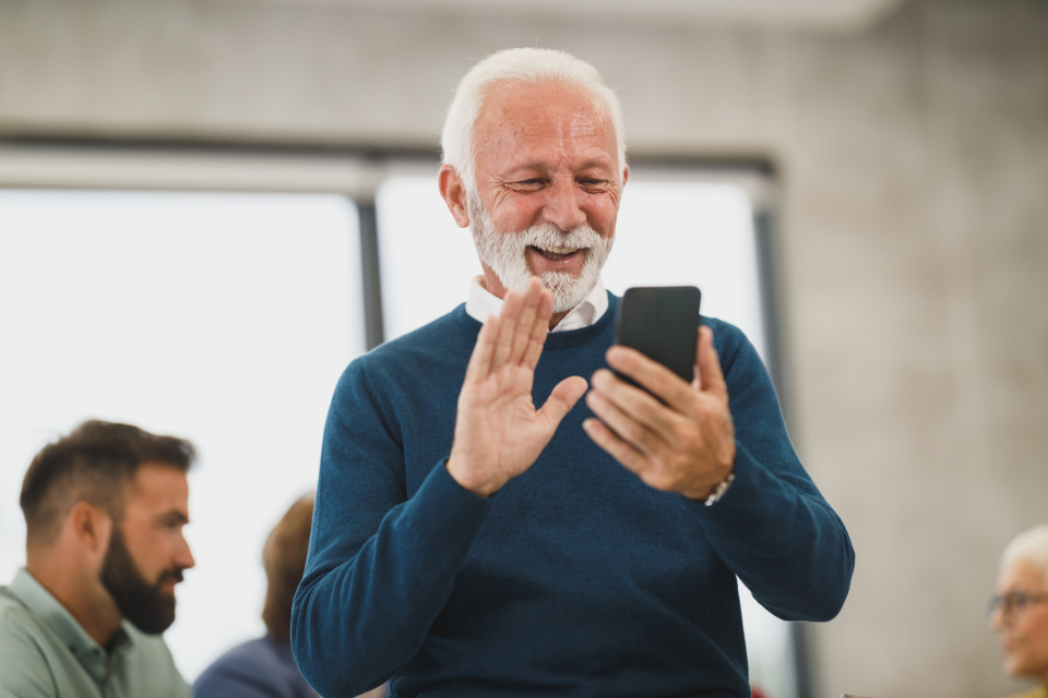 An older man smiling and waving on a video call on his phone