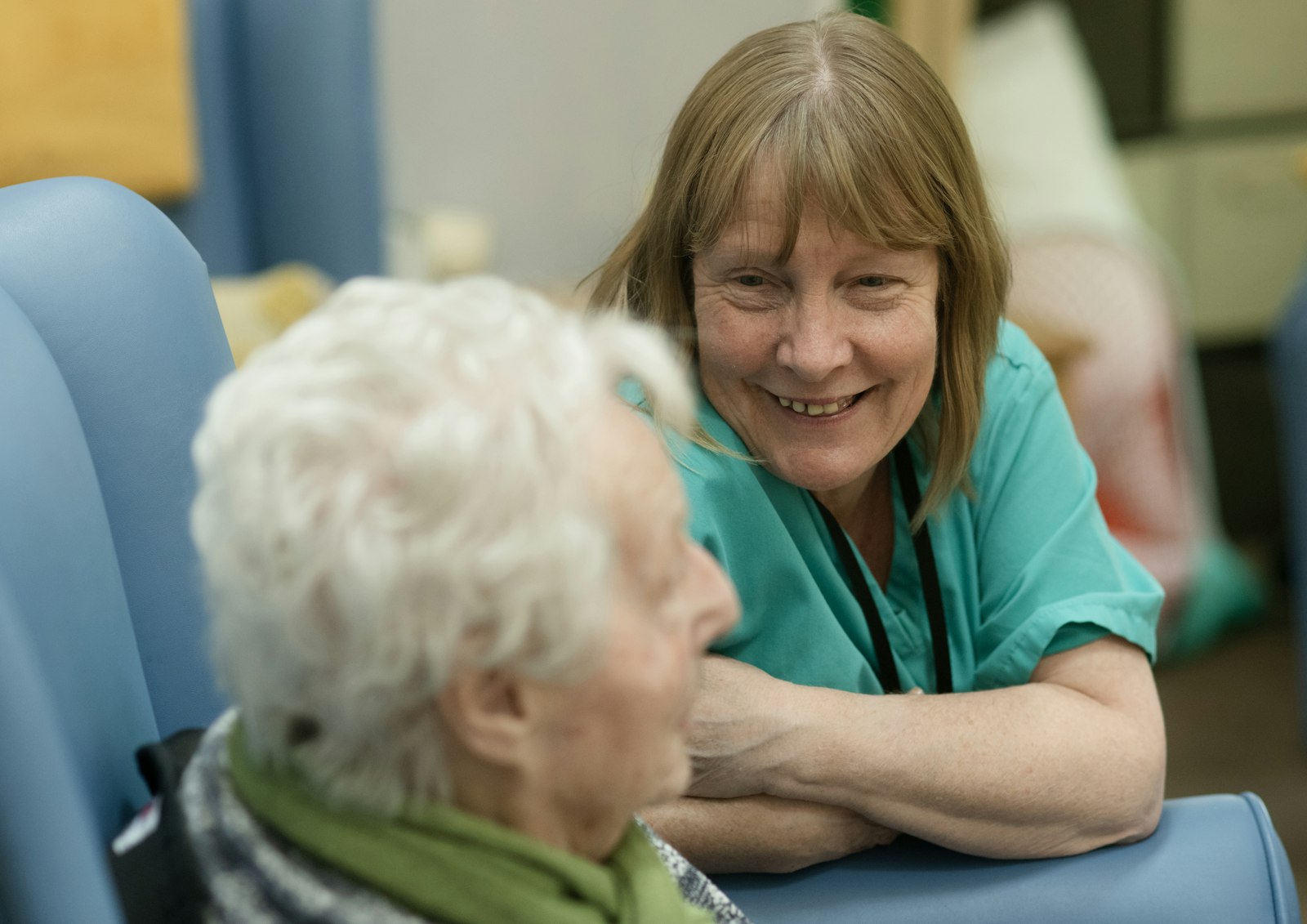 A smiling carer sitting with an older woman, the two of them talking warmly