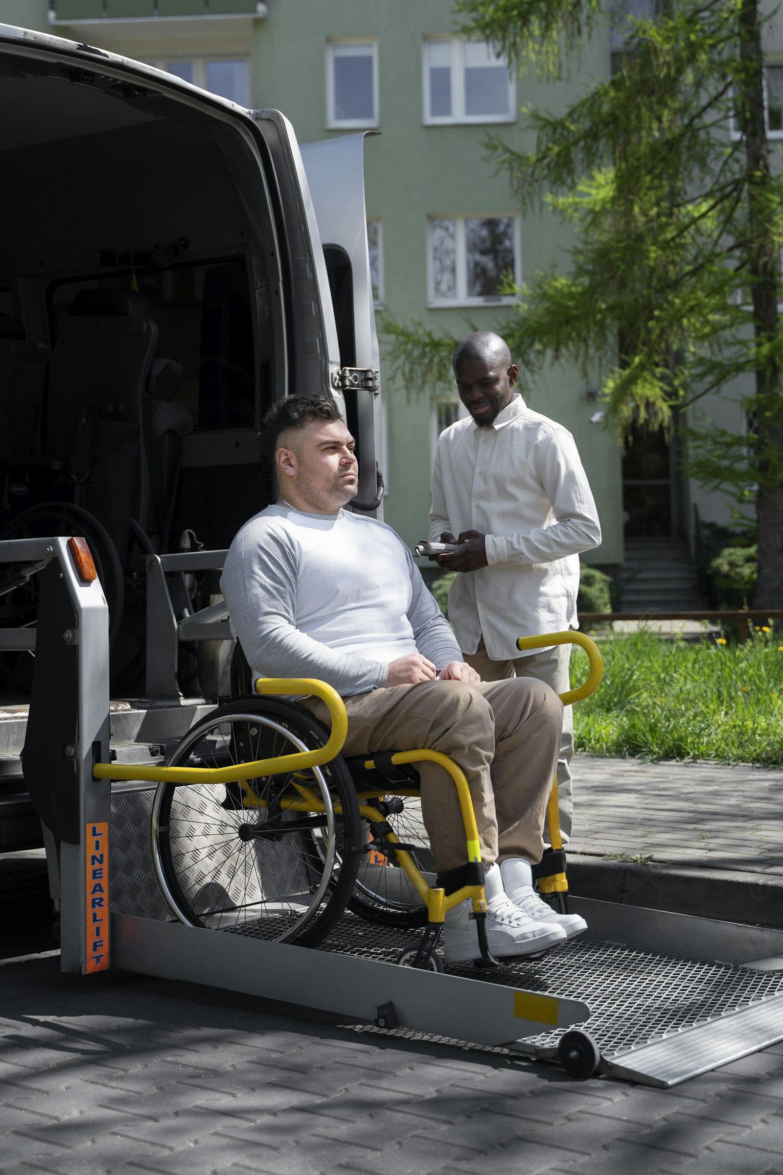 A man in a wheelchair on the lift of an accessible van with a support worker beside him